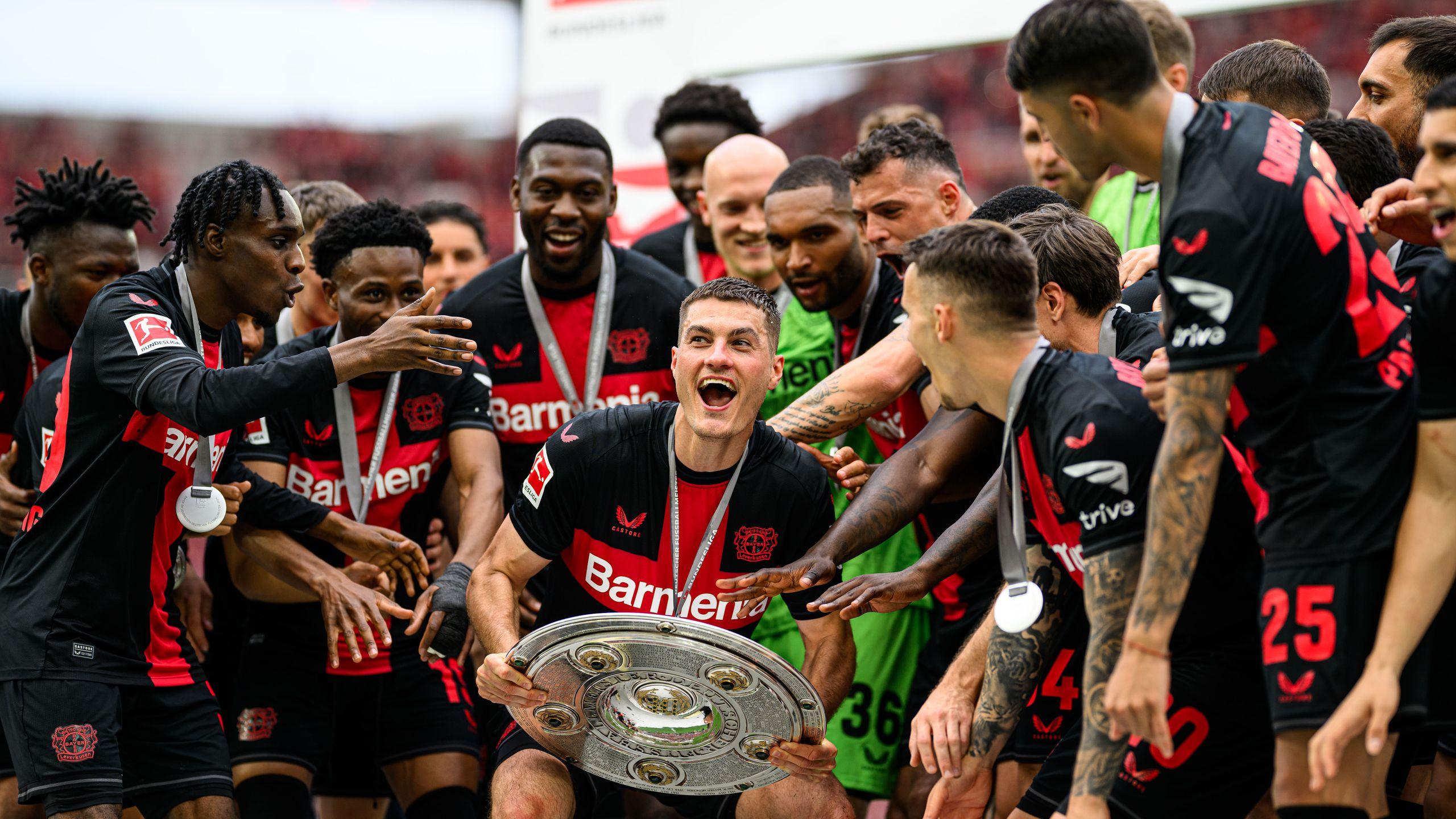Mehrere Fußballspieler stehen im Halbkreis und sammeln sich um einen Spieler der voller Freude den Pokal hält.