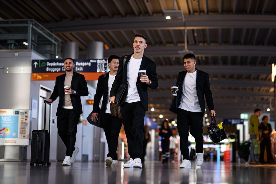 4 Fußballer in Sakkos laufen im Flughafen mit Tasche und Kaffee entlang