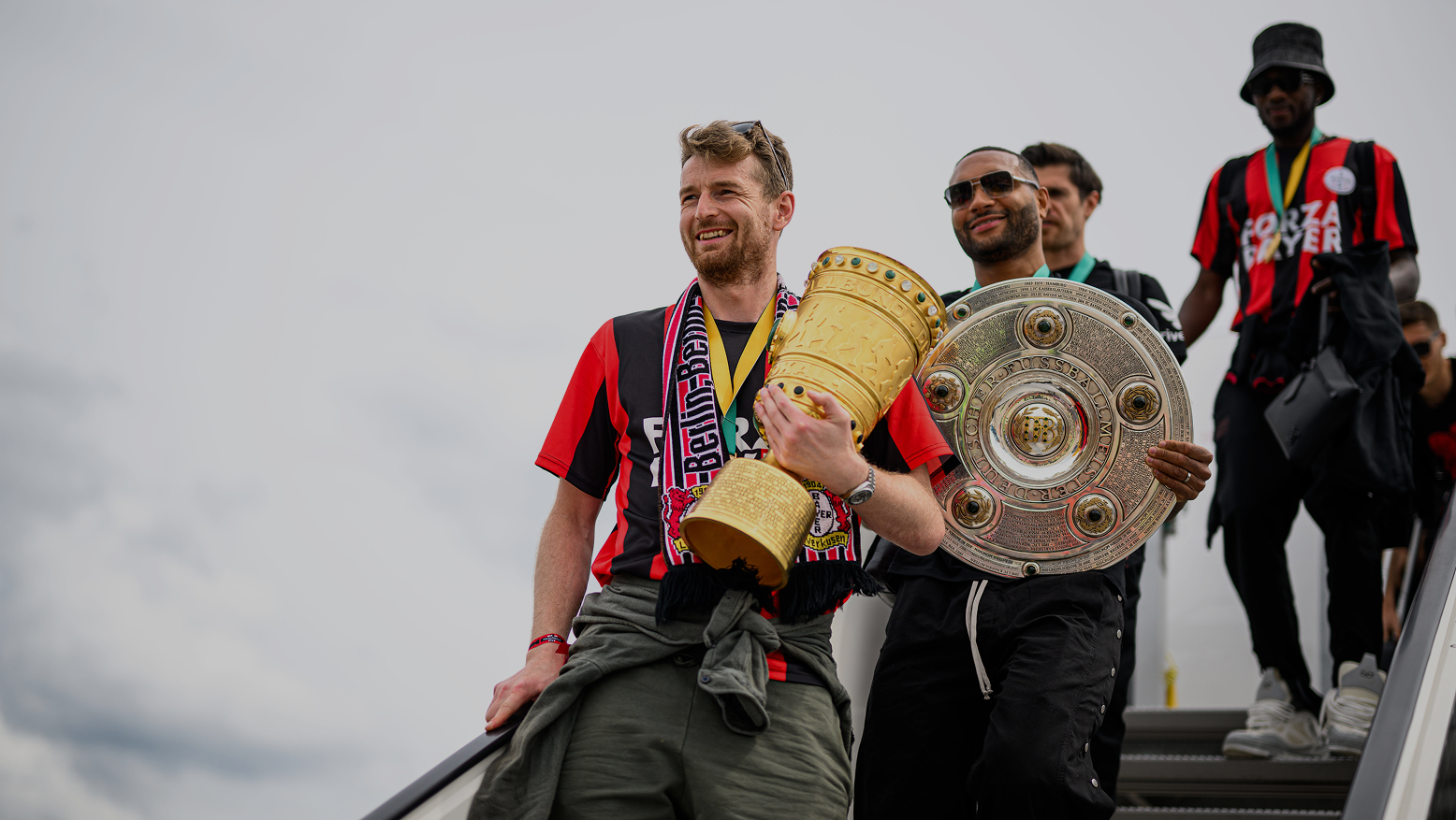 Bayer Leverkusen Fußballspieler läuft mit Pokal aus dem Flugzeug.